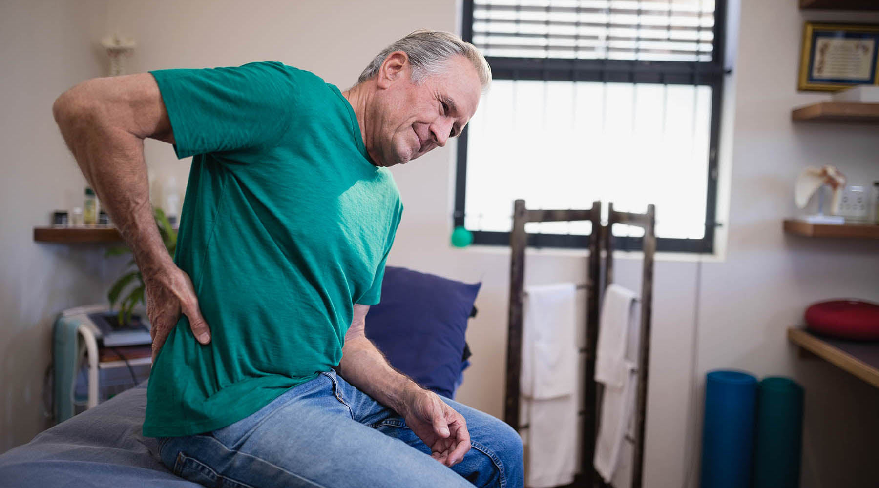 Older man in green shirt at doctor's office dealing with pain from tension myalgia