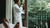 Man with hair pulled back in a white robe looking out the window and drinking coffee after a sexual encounter