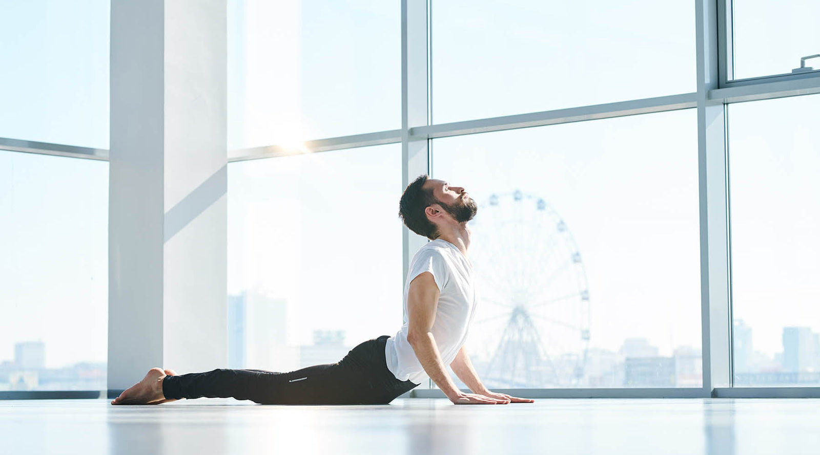 Man in white shirt and black pants performing Kegel exercises in a room with big windows
