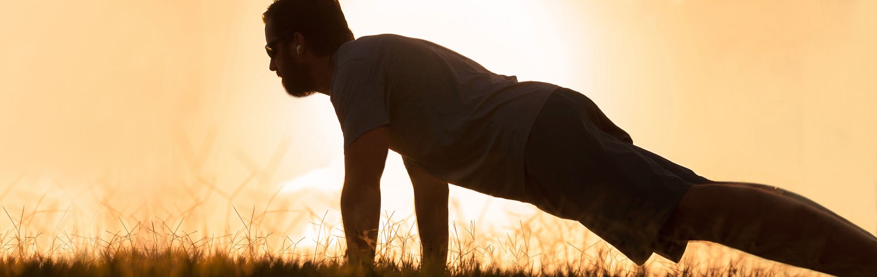 Healthy looking man holding a plank position in front of a sunset