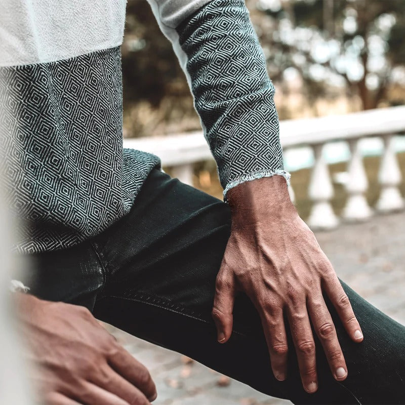 Midsection photo of man in gray two-tone sweater and black jeans with hands on inner thighs
