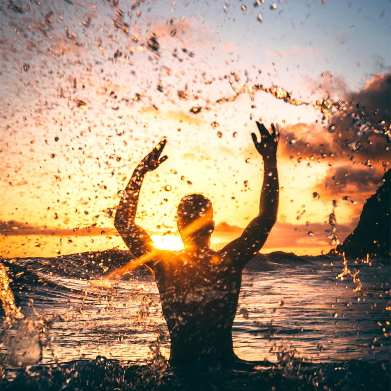 Man in water with hands in the air, splashing water at sunset
