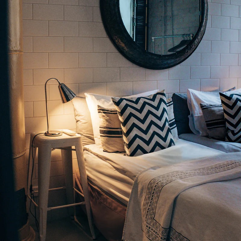 Bedroom scene with white tile wall, round mirror, white bed sheets and pillows 